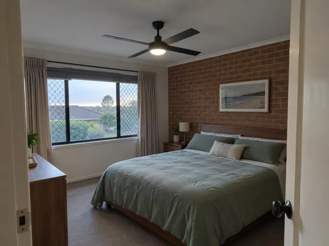 Bedroom with a black ceiling fan above a bed, brick feature wall and window in Kanwal
