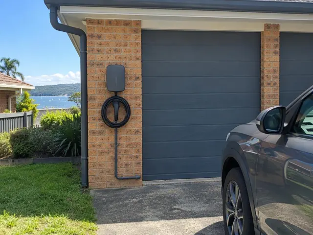 EV charger mounted on a brick garage wall beside a dark roller door in Gwandalan